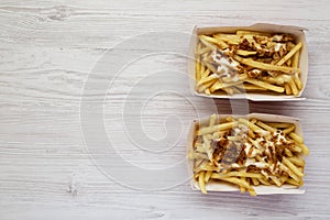 French fries with cheese sauce and fried onion in paper boxes on a white wooden table, top view. Flat lay, from above, overhead.