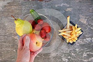 French fries, fruits, vegetables on old wooden background. Concept choosing correct nutrition or of junk eating.