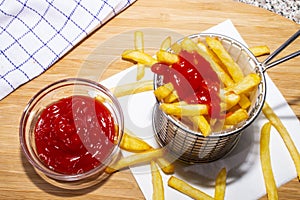 French fries in a metal basket and ketchup in a glass bowl