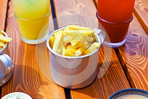 French fries in metal cup and lemonades on brown boards wooden table. Fastfood, potato. Outdoor cafe on street, sidewalk