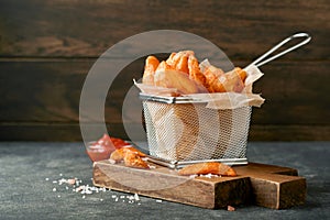 French fries in metal wire basket with salt and ketchup on old wooden dark background clous up. Fried potatoes. Fast food