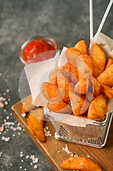 French fries in metal wire basket with salt and ketchup on old wooden dark background clous up. Fried potatoes. Fast food