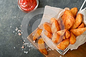 French fries in metal wire basket with salt and ketchup on old wooden dark background clous up. Fried potatoes. Fast food