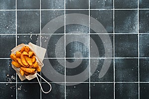 French fries in metal wire basket with salt and ketchup on old wooden dark background clous up. Fried potatoes. Fast food