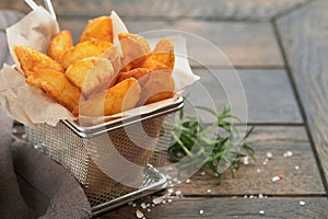 French fries in metal wire basket with salt and ketchup on old wooden dark background clous up. Fried potatoes. Fast food and