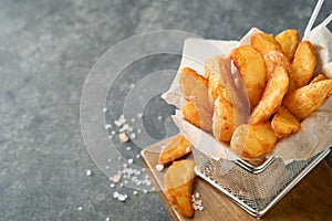 French fries in metal wire basket with salt and ketchup on old wooden dark background clous up. Fried potatoes. Fast food