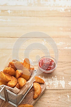 French fries in metal wire basket with salt and ketchup on old wooden light background clous up. Fried potatoes. Fast food