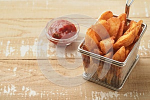 French fries in metal wire basket with salt and ketchup on old wooden light background clous up. Fried potatoes. Fast food