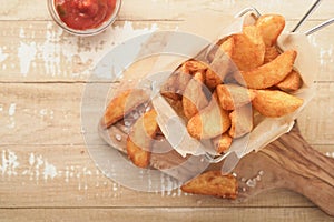 French fries in metal wire basket with salt and ketchup on old wooden light background clous up. Fried potatoes. Fast food and