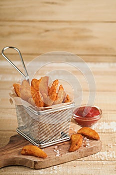 French fries in metal wire basket with salt and ketchup on old wooden light background clous up. Fried potatoes. Fast food