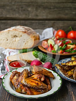 French fries, salad, vegetables on an old wooden background. Rural dinner, summer picnic. Close up