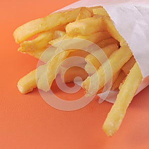 french fries in white paper bag on orange background. fast food