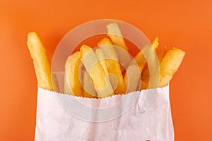 french fries in white paper bag on orange background. fast food