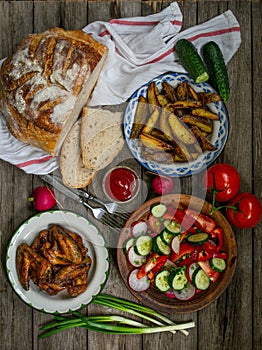 French fries, wings, salad, vegetables, bread on an old wooden background. Rural dinner, summer picnic. Top view. Flat lay