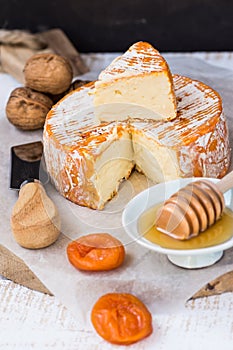 French or German soft cheese of camembert type with orange rind, honey dipper, dried fruits, knife