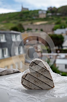 French heartshaped neufchatel cow cheese on white paper and view on old houses of Etretat, Normandy, France