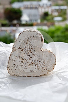 French heartshaped neufchatel cow cheese on white paper and view on old houses of Etretat, Normandy, France