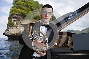 French horn player. Hornist playing brass orchestra music instrument. Portrait against the backdrop of the sea landscape