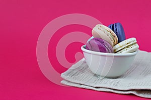 French macaroons in cup. Front view. Sweet colorful macaroons. Sweet bisquits. Hot pink background. Table cloth.