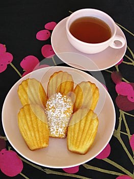 French madeleines and tea in pink vintage dishware on black and magenta cherry-pattern tablecloth