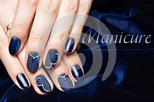 French manicure - beautiful manicured female hands with blue manicure with rhinestones on dark blue background