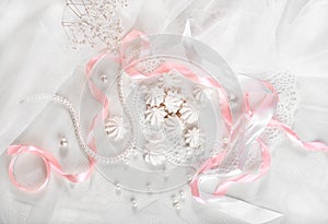 French meringue cookies for wedding background with pearls, pink and white satin ribbons and lace, flat lay