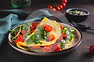 French omelette filled with cherry tomatoes and arugula on a plate on the table
