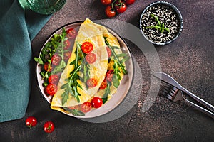 French omelette filled with cherry tomatoes and arugula on a plate on the table top view