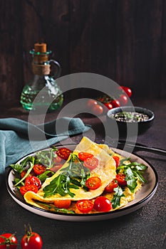 French omelette filled with cherry tomatoes and arugula on a plate on the table vertical view