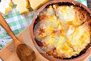 French onion gratin soup in a clay pot, authentic recipe, wooden spoon on a cutting board on an old rustic table, close-up