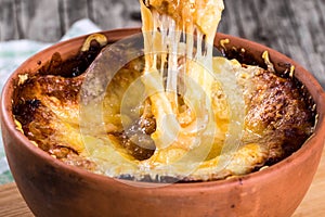 French onion gratin soup in a clay pot, authentic recipe, wooden spoon on a cutting board on an old rustic table, close-up