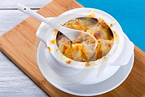 French onion gratin soup in a white pot, close-up