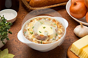 French onion soup in a white ceramic bowl on a brown table with ingredients.