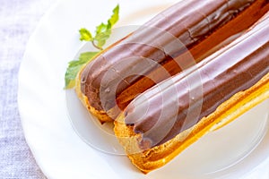 French pastry eclairs with cream filling covered with melted milk chocolate and mint leaves