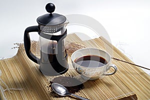 French press coffee with cup of coffee and coarse coffee powder on wooden pedestal white background