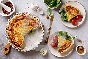 French quiche Lorraine cut into slices and served on plates with tomatoes and herbs