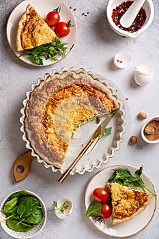 French quiche Lorraine cut into slices and served on plates with tomatoes and herbs