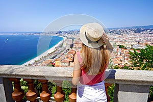 French Riviera. Back view of beautiful young woman holding hat enjoying the cityscape of Nice, France