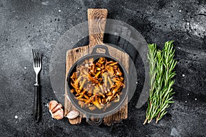 French roasted chanterelle mushrooms with onions and thyme in a pan. Black background. Top view