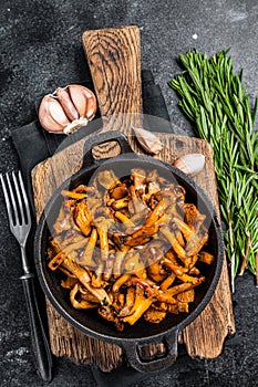 French roasted chanterelle mushrooms with onions and thyme in a pan. Black background. Top view