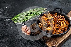 French roasted chanterelle mushrooms with onions and thyme in a pan. Black background. Top view. Copy space