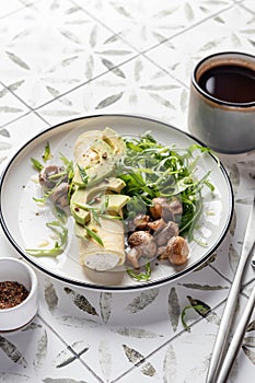 French rolled omelette stuffed with cream cheese with avocado, aragula and mushrooms for breakfast on white plate