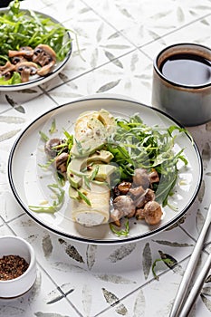 French rolled omelette stuffed with cream cheese with avocado, aragula and mushrooms for breakfast on white plate