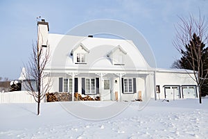 French-style clapboard house with dormer windows, black shutters and porch seen after fresh snowfall