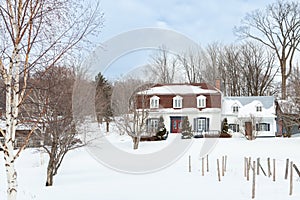 French-style patrimonial white double house with shingles and metal roof in a snowy land