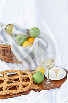 French style romantic picnic setting. Set of cheese, wine, apple, dry bread. Blanket, white sheets with food prepared for summer