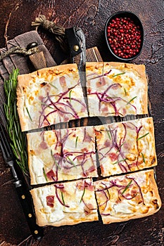 French tarte flambee with cream cheese, bacon and onions. Flammkuchen from Alsace region. Dark background. Top view