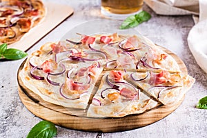 French tarte flammkuchen with cream cheese, onion and bacon on a board on the table