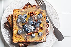 French toast with blueberries, pecan and maple syrup for breakfast on white plate