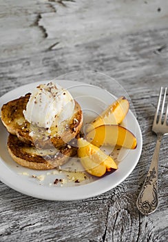 French toast with vanilla ice cream, honey, nuts and peaches on a white plate